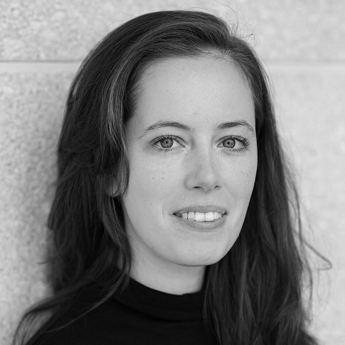 Frau mit langen, dunklen Haaren trägt schwarzen Rollkragenpullover vor heller Wand.