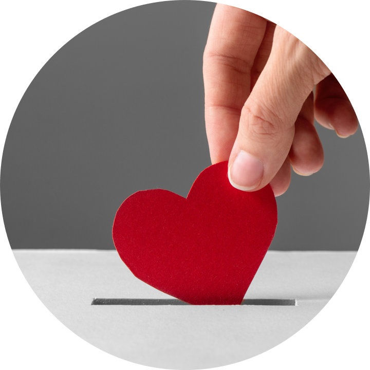 Hand legt rotes Papierherz in einen Schlitz einer Spendenbox.