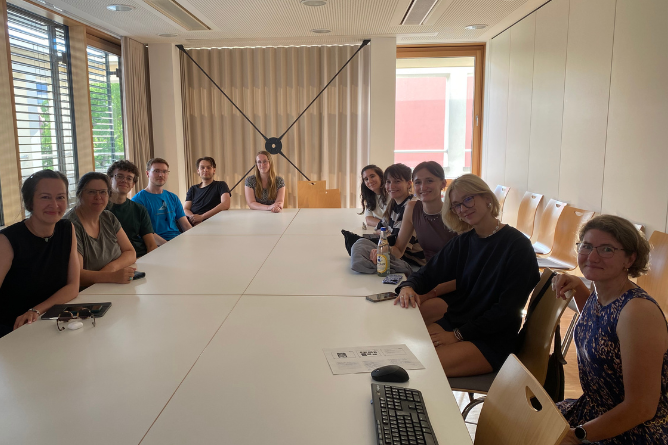 ACHSE am UKKD Gruppe von Studierenden sitzt an einem langen weißen Tisch in einem hellen Raum mit Fenster und Vorhang